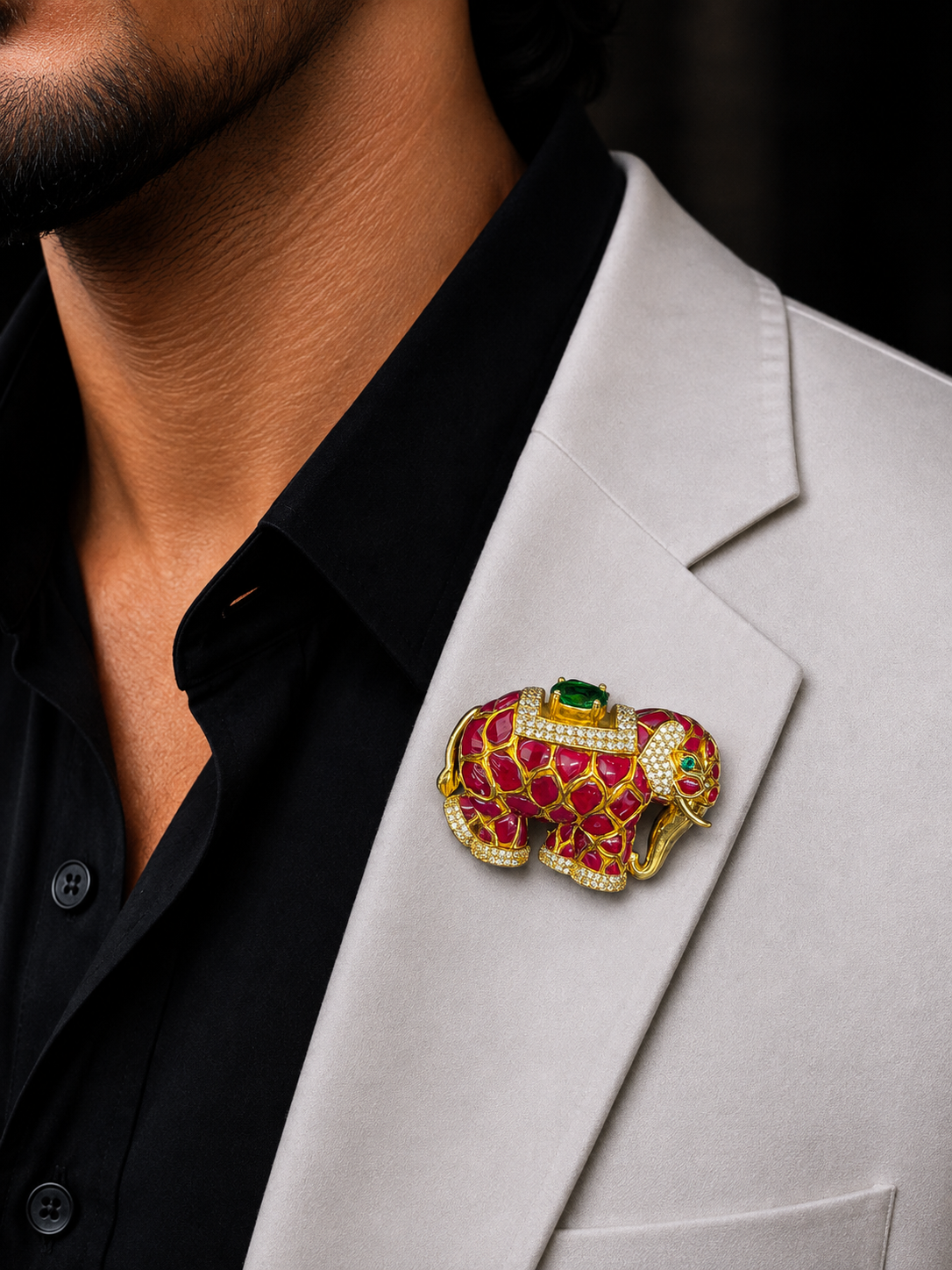 A gold elephant-shaped lapel pin with red enamel, white rhinestones, and a green jewel, worn on a man's light gray blazer over a black shirt.