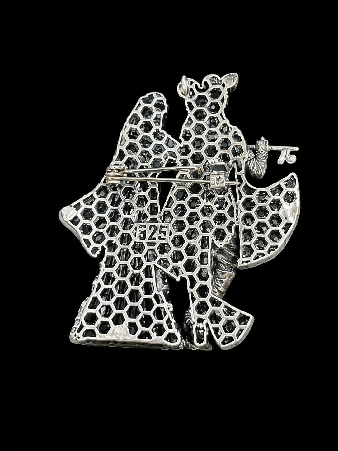 A silver filigree brooch depicting two stylized figures, one holding a small flower, with a visible 'S225' hallmark on the center, set against a solid black background.